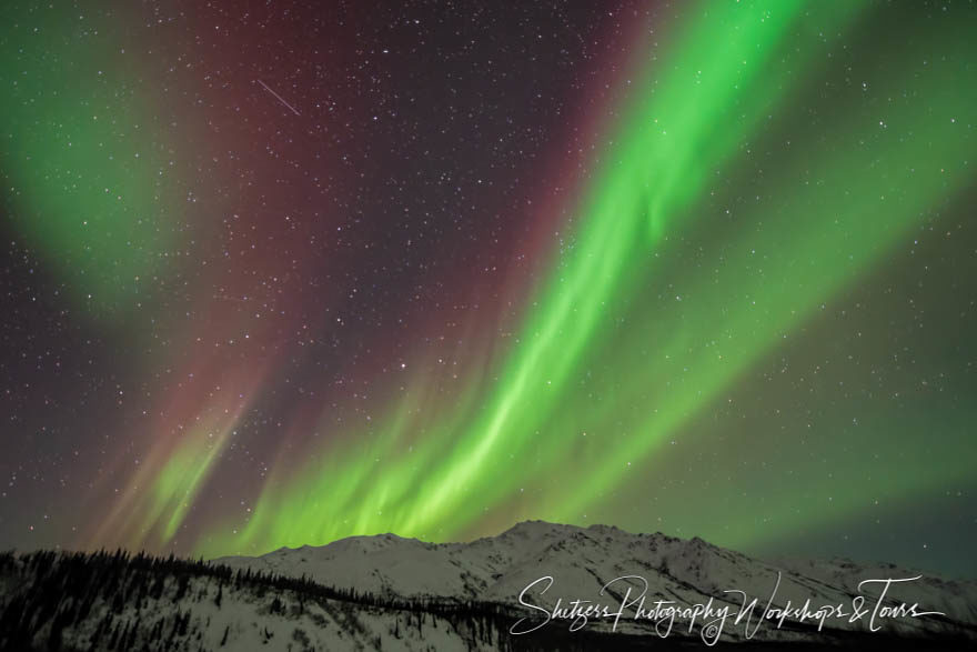 Aurora Borealis streams purple and green light over jagged mount