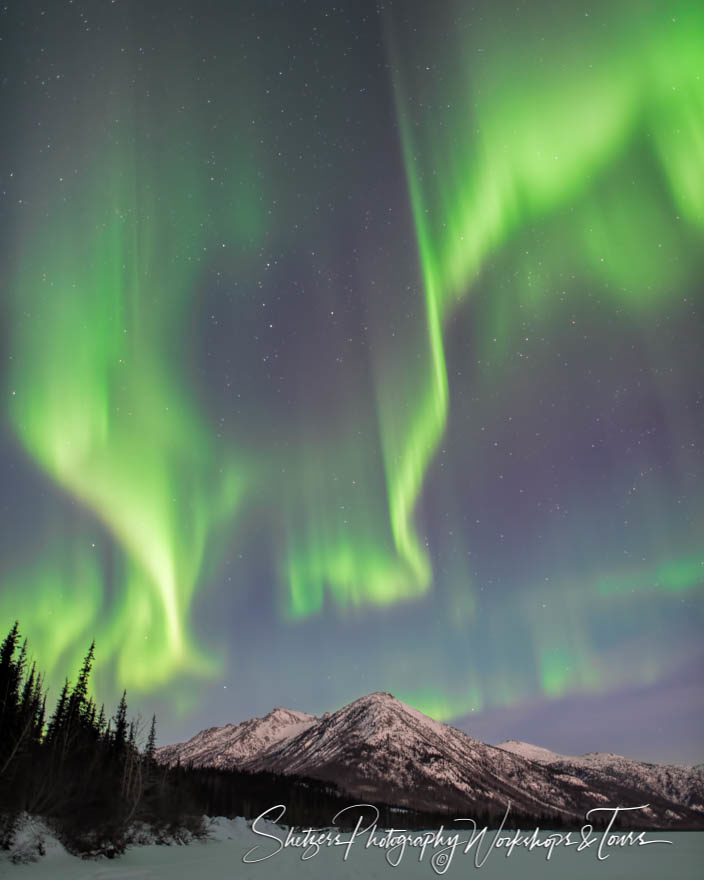 Dancing Northern Lights glow green over mountain peaks