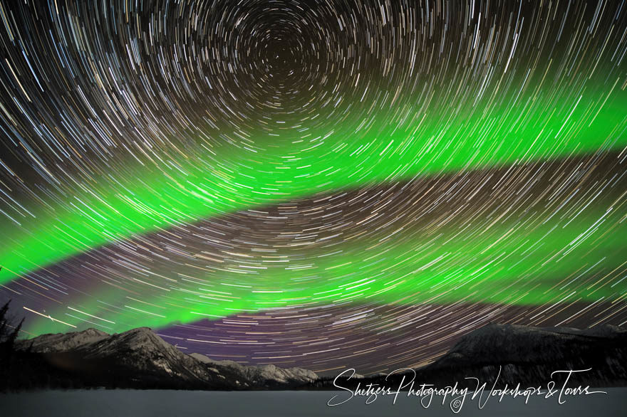 Northern lights with star trails illuminate mountain peaks