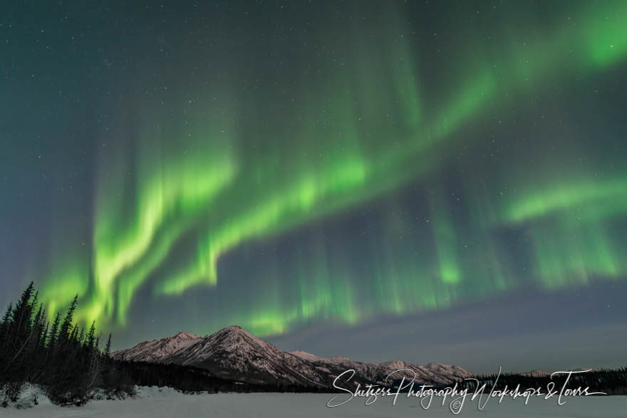 Waves of light illuminate night sky above mountains